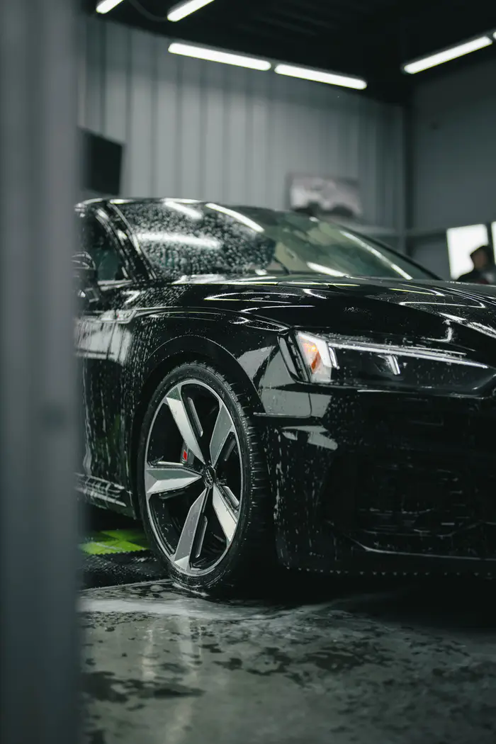 Black Audi RS5 front-quarter and wheel photograph with indoor light reflections