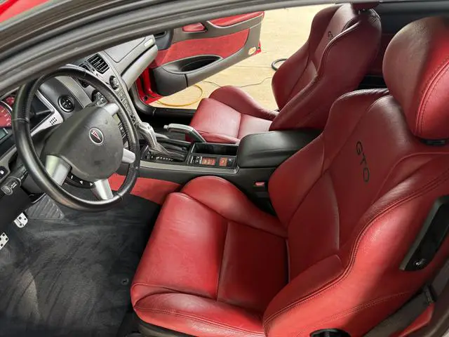 Red leather interior of a Pontiac GTO after detailing, with conditioned bucket seats and a polished center console