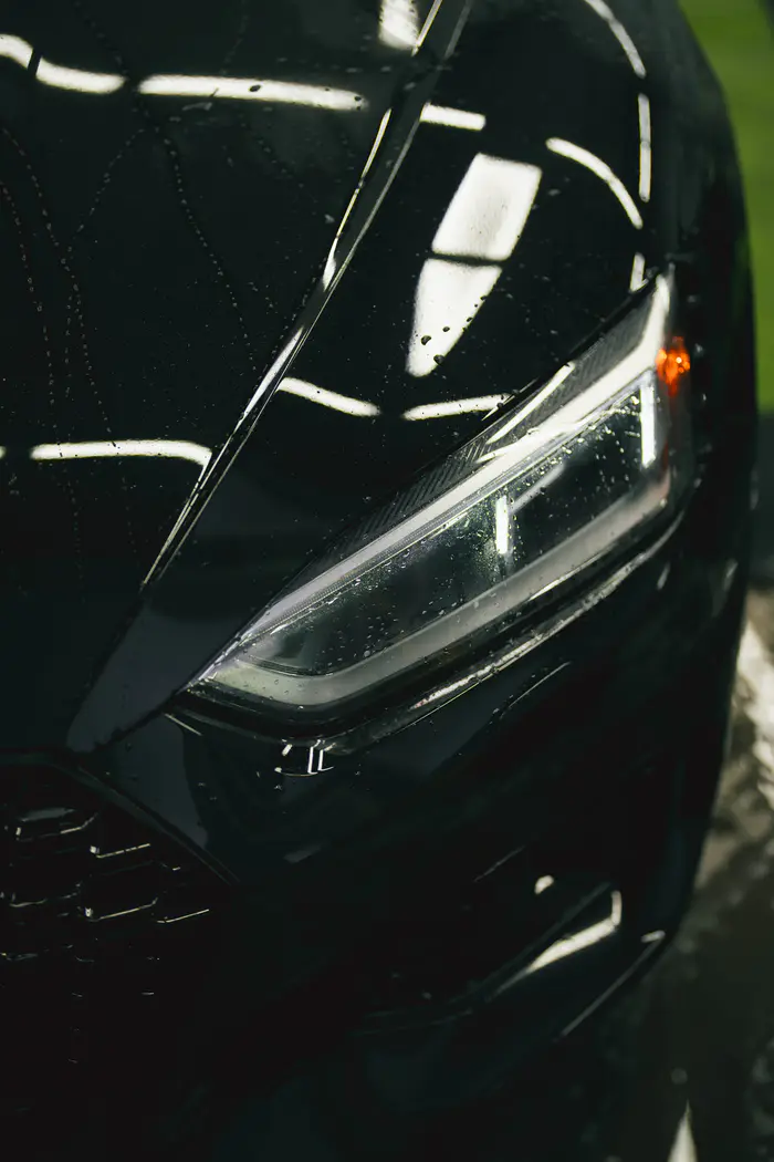 Black Audi RS5 hood and headlight with curved overhead-light reflections