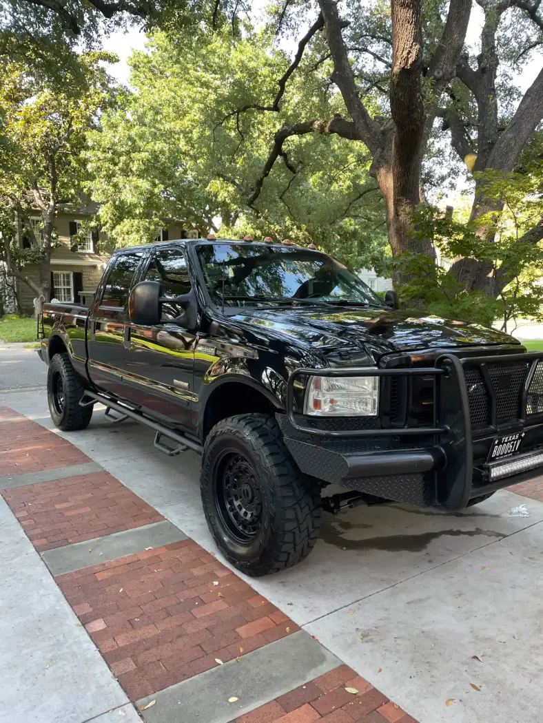 Black Ford pickup truck parked on a driveway with trees and houses in the background.