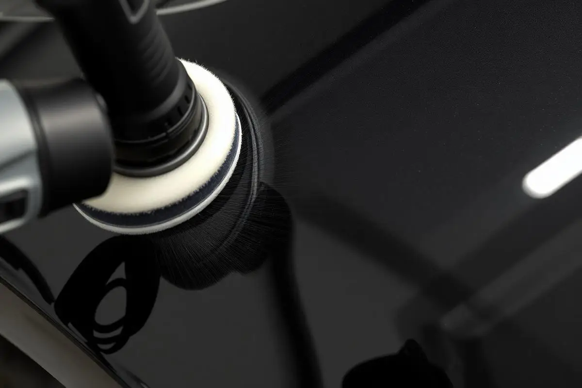 Machine polisher removing swirl marks from black car paint