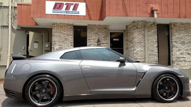 Gray Nissan GT-R sports car parked in front of a building with DTI sign.