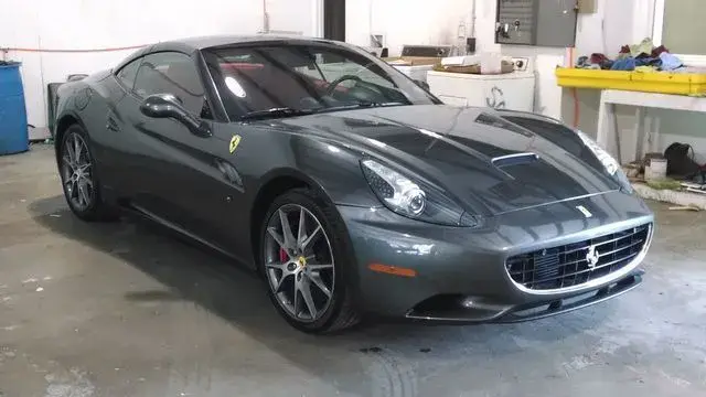 Dark gray Ferrari sports car in a garage with red brake calipers.