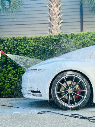 Car being washed with foam and water spray in driveway