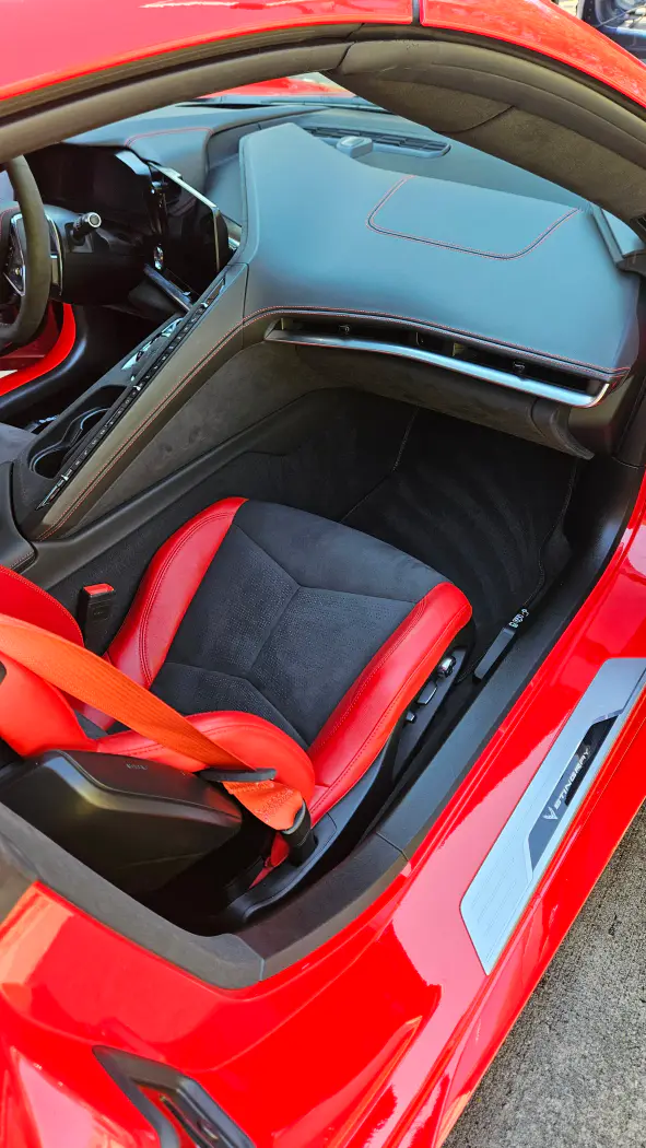 Interior view of a red Chevrolet Corvette Stingray, featuring a racing seat with a red seatbelt, dashboard, and center console.