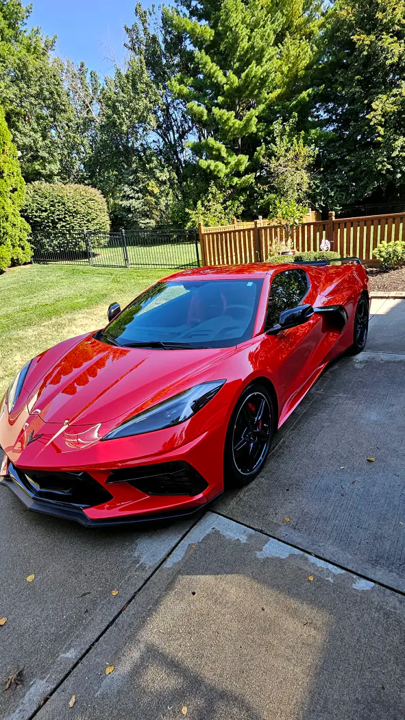 Red Chevrolet Corvette parked on a driveway with a backyard and green trees in the background.