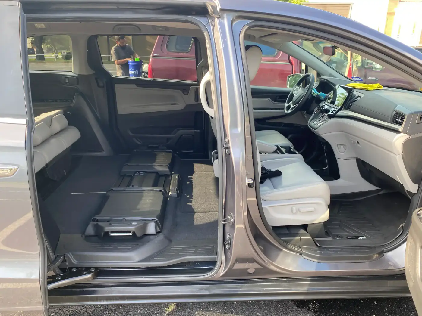 Inside of a vehicle with the seats folded down and the dashboard visible, parked in a lot with other vehicles and a person in the background.